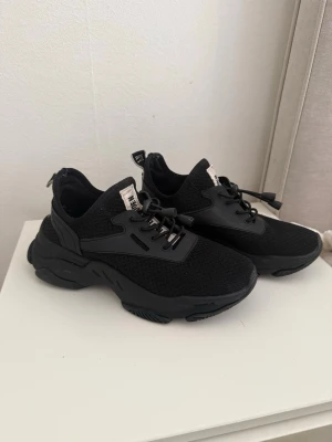 Svarta Steve Madden skor - Snygga svarta sneakers med chunky sula och meshdetaljer. Skorna har svarta snören och dragflik bak samt en vit etikett på plösen. 