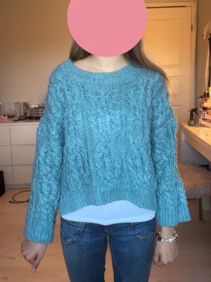 Blå chunky stickad tröja - Mysig blå chunky stickad tröja med grovt kabelstickat mönster och breda muddar. Tröjan har en avslappnad passform, rund halsringning och är perfekt för kyliga dagar. Passar till jeans eller kjol för en casual look.