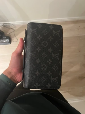 Louis Vuitton svart monogram plånbok - Snygg svart plånbok från Louis Vuitton med klassiskt monogrammönster i grått. Tillverkad i tåligt läder med rektangulär form och smart knappstängning på sidan. Perfekt för dig som gillar exklusiva accessoarer med ikonisk design. Precis som ny, använd få gånger. 