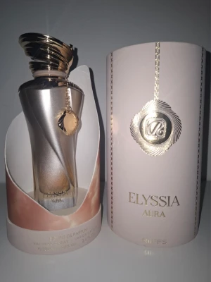 Elyssia Aura Extrait de Parfum - Detta är en ny doft, lanserades 2026. Toppnoterna är Apelsin, Muskot och Kanel; hjärtnoterna är Vanilj, Grädde, Kakaoböna och Cognac; basnoterna är Patchouli, Vanilj och Cederträ.  Säljes pga downsizing - skriv innan köp!