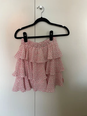 Blommig volangkjol - Rosa och vit blommig kjol från Kiss The Sky i strl XS. Köpt begagnad så tror den är rätt så använd men är ändå i jättefint skick, inte nopprig eller något speciellt jag sett