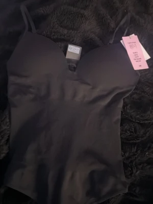 Svart shaping-body från H&M - Snygg svart shaping-body från H&M med tunna justerbara axelband och vadderade kupor. Tillverkad i ett stretchigt material som formar kroppen.