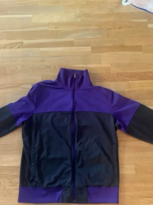 Nike sportswear track jacket- Lila/Svart (Large) - Säljer en riktigt snygg träningsjacka från Nike Sportswear i en cool färgblockerad design med härliga retrovibbar. Modellen ger en skön 90- talslook med sin höga krage, hela dragkedja och sportliga passform.  Perfekt för en avslappnad streetwear-stil eller till träningen.                                  Kom gärna med frågor eller prisförslag!