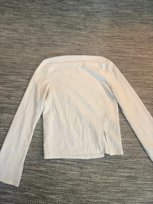 Topp/ tröja Gina Tricot - Säljer en stilren vit offshoulder topp från Gina Tricot i storlek S. Toppen har långa ärmar som öppnas vid slutet. Perfekt att matcha med både jeans och kjol för en trendig outfit.