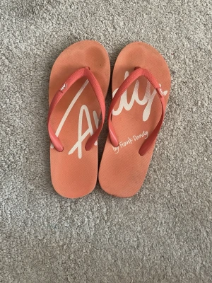 Rosa flip-flops från Frank Dandy - Snygga rosa flip-flops från Frank Dandy med vit logga på ovansidan. Tillverkade i mjukt gummi med klassisk tårem och platt sula. Perfekta för sommaren och stranden. Storlek 37, går inte att trycka in den storleken 