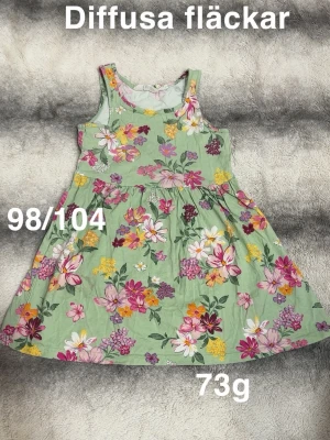 Grön blommig ärmlös klänning - Söt grön klänning med färgglatt blommönster i rosa, gult, vitt och lila. Klänningen är ärmlös och har en rund halsringning. Perfekt för varma dagar och har en lätt, 🌸 Diffusa fläckar. Storlek 98/104