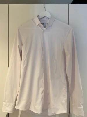 Vit klassisk skjorta från Zara - Stilren vit skjorta slimfit från Zara med klassisk krage och långa ärmar. Skjortan har en rak passform och knäppning framtill. Perfekt till både jeans och kostymbyxor för en clean look. Skjortan är väldigt mjuk och skön samt behöver nästan aldrig strykas. 