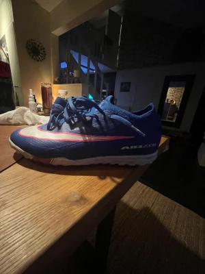 Blåa Nike Air Zoom fotbollsskor PRO  - Säljer ett par blåa Nike Air Zoom PRO fotbollsskor med vit och rosa swoosh på sidan. Skorna har snörning och låg profil, perfekt för snabba rörelser på planen. Ovandelen är i syntetmaterial och sulan är designad för bra grepp på konstgräs och grus. Målfarlig sko för dig som vill ha det lilla extra självförtroendet på planen 