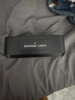 Svart digital väckarklocka - Säljer en svart digital väckarklocka med snooze- och ljusfunktion. Klockan har flera knappar för att ställa in tid, datum, alarm och temperatur i både Celsius och Fahrenheit. Enkel och smidig design som passar på nattduksbordet.