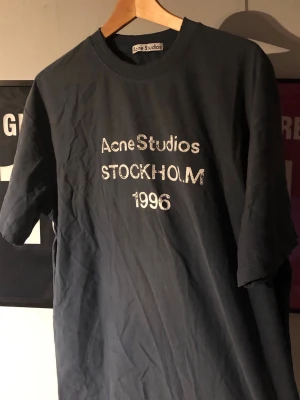 Mörkblå Acne Studios t-shirtÖPPEN FÖR BUD - Cool svart t-shirt från Acne Studios med vit text 'Acne Studios STOCKHOLM 1996' på bröstet. Klassisk rund hals och korta ärmar. Tillverkad i mjuk bomull för en skön känsla och avslappnad passform.