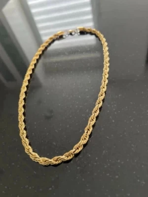 Flätat guldhalsband - Snyggt halsband i guldfärgad metall med flätad kedja som ger en cool och trendig look. Perfekt för att lyfta vilken outfit som helst med sin unika design och glänsande finish. Låset är i silverfärg och halsbandet har en klassisk form.