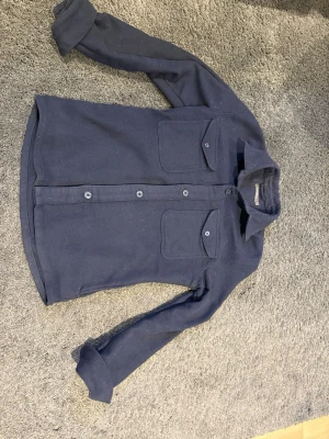 Mörkblå overshirt med fickor Dressman - Stilren mörkblå overshirt med två stora bröstfickor med lock och knappar. Skjortan har klassisk krage, raka ärmar och knäppning framtill. Materialet ser ut att vara mjukt och lite tjockare, perfekt för lager på lager. Enkel och clean design som passar till det mesta. Från Dressmann, passar bra på mig är 175 och 65 kilo sitter perfekt.