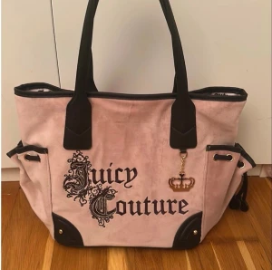 Rosa Juicy Couture handväska - Säljer en rosa handväska från Juicy Couture i mjukt sammetstyg med svarta detaljer och handtag. Väskan har broderad logga framtill och en guldfärgad kron-charm. Stor och rymlig som passar som handväska för flyget eller skolväska. Ny och oanvänd.