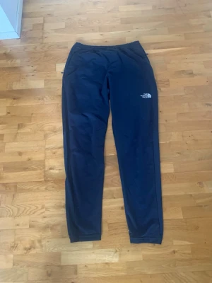 Svarta mjukisbyxor från The North Face - Säljer ett par svarta mjukisbyxor från The North Face med logga på både fram- och baksidan. Byxorna har smal passform, resår i midjan och muddar vid bensluten. Perfekta för chill eller träning, tillverkade i mjukt och stretchigt material.