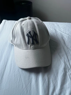 Beige New York Yankees keps - Snygg beige keps med New York Yankees-logga i svart framtill. Klassisk böjd skärm och justerbar rem baktill. 