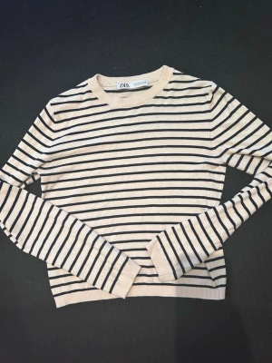 Randig tröja från Zara, beige/svart - Snygg långärmad tröja från Zara i beige med svarta horisontella ränder. Tröjan har rund halsringning och är gjord i ett mjukt, tunt material som passar perfekt till lager på lager. Klassisk och enkel design som funkar till mycket.