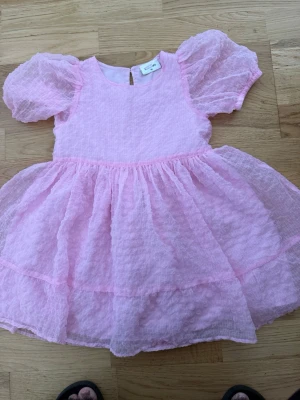 Ljusrosa puffärmad kortklänning - Supersöt ljusrosa kortklänning från Kappahl med puffiga korta ärmar och volangkjol. Klänningen har en lätt strukturerad yta och rund halsringning. Perfekt för dig som vill ha en gullig och trendig look.