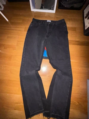 Flared Jeans - Säljer ett par svarta jeans med rak passform och rå, fransig kant nedtill. Jeansen har klassisk femficksdesign och är tillverkade i ett kraftigt denimtyg. Perfekta för en avslappnad och trendig look.