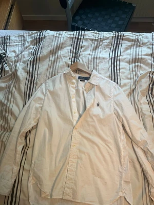 Vit skjorta från Polo Ralph Lauren - Klassisk vit skjorta från Polo Ralph Lauren i slim fit-modell. Skjortan har lång ärm, knappar framtill och den ikoniska broderade loggan på bröstet. Tillverkad i mjuk bomull som känns skön mot huden. Perfekt för en clean och stilren look.