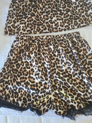Leopardmönstrad pyjamas med spets - Säljer ett set med pyjamaslinne och shorts i glansigt material med leopardmönster. Shortsen har elastisk midja och svart spetskant nedtill. Perfekt för dig som gillar djurmönstrat och vill ha något bekvämt och snyggt att chilla i.