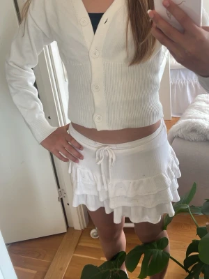 Vit  kofta med knappar - Säljer en vit cropped kofta med v-ringning och stora knappar framtill. Koftan har långa ärmar och ribbstickad midja som ger en snygg passform. Perfekt att matcha med kjol eller jeans för en trendig look.