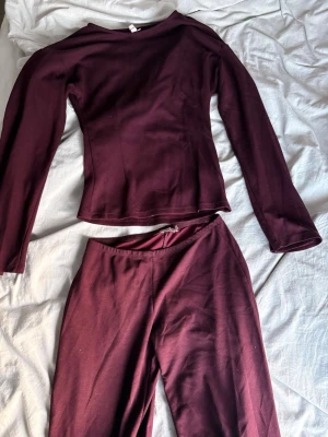 Vinrött set med långärmad topp - Säljer ett vinrött set med långärmad topp och matchande byxor från Nelly. Setet är i mjukt, stretchigt material och har en enkel, stilren design utan synliga detaljer eller mönster. 