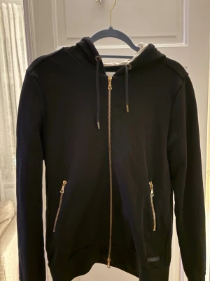 *EXKLUSIV* Limitato Hoodie  - En Limitato Hoodie med dragkedja i guld och två fickor framtill. Insidan av huvan är vit och baksidan har ett stort fototryck med en man i hatt. Snygga detaljer och cool look, perfekt för dig som gillar streetstyle. Pris kan diskuteras!