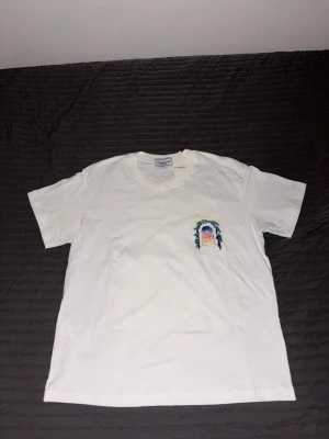 Vit t-shirt från Casablanca med tryck - Jag Säljer denna Vit t-shirt från Casablanca,  eftersom den tyvärr aldrig riktigt blivit använd i min garderob. Den är i fantastiskt skick, men den passar inte min stil, så den förtjänar att få en ny användare mer än vad jag gör. Perfekt för dig som vill ha en kvalitets-basic med lyxig känsla!