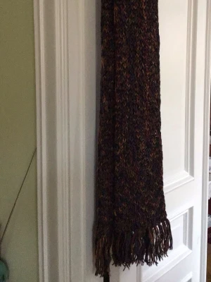 Flerfärgad stickad halsduk med fransar - Mysig stickad halsduk i flera färger som svart, vinröd, gul och blå. Halsduken har en chunky struktur och avslutas med långa fransar i samma färgskala. Perfekt för att ge din outfit en färgklick och hålla dig varm under kalla dagar.