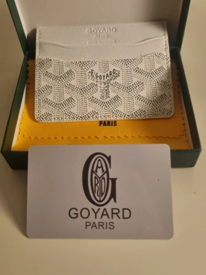 Vit kortfodral från G4yard - Snyggt vitt kortfodral från G4yard med det klassiska mönstret och logotyp framtill. Tillverkat i exklusivt läder och har flera fack för kort. Kommer i originalask med tillhörande tyg och certifikat. Perfekt accessoar för dig som gillar lyxiga detaljer.