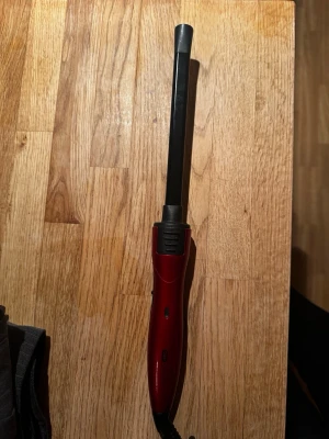 Röd locktång med smalt stavformat järn - Säljer en röd locktång med smalt, svart stavformat värmeelement och ergonomiskt handtag. Tången har en på/av-knapp och är sladdansluten. Perfekt för att fixa lockar eller vågor i håret. Passar dig som vill ha ett enkelt stylingverktyg. Medföljer två finger vantar. 