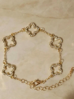 Guldigt armband med fyrklöver✨ - Snyggt armband i guldfärg med fem fyrklöverformade länkar, dekorerade med gnistrande stenar runt kanterna. Justerbar kedja och karbinlås gör det enkelt att anpassa storleken. Perfekt accessoar för dig som gillar bling och trendiga detaljer✨🫶