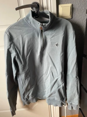 Grå halvzip sweatshirt från mottis - En grå  sweatshirt med halv dragkedja. Tröjan har ett litet broderat emblem på bröstet och ribbade muddar vid ärmslut och nederkant. .