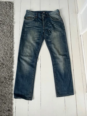 D&G blå jeans med brodyr - Snygga blå jeans från D&G med raka ben och slitningar framtill. Baksidan har stora broderade D&G-bokstäver i gult och blått, samt två bakfickor. Klassisk femficksmodell i denim med cool vintagekänsla.