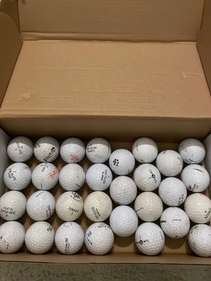 Låda med blandade golfbollar - En stor låda fylld med vita golfbollar av olika märken och modeller. Bollarna har klassisk rund form och är tillverkade i slitstarkt material med dimple-mönster för bättre flygförmåga. Perfekt för dig som vill fylla på golfutrustningen med många bollar.