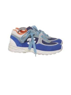 Blå och vita sneakers från Chanel - Snygga sneakers från Chanel i blått, vitt och grått med ljusblå skosnören och orange detalj på insidan. Skorna har en klassisk låg siluett och är tillverkade i en mix av mocka och textil. Perfekta för dig som vill ha en sportig och trendig look.