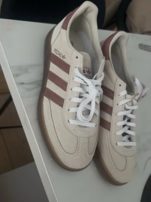 Adidas Spezial beige/bruna sneakers - Säljer ett par helt nya adidas spezial. Säljer då jag fick fel färg än den jag beställt. Så jag är lite osäker på vad färgen heter men de är kräm vita med rosa sträck. Aldrig använda storlek 39 1/3. Passar mig som vanligtvis har 39. Köpta för ca 1300 och säljer för 1100. Skickas original förpackning. Hör av dig vid frågor🩷