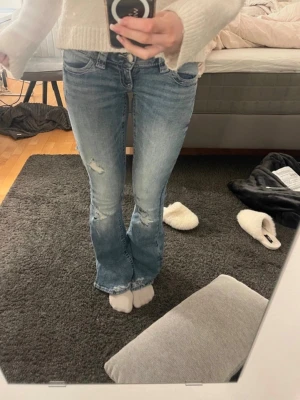 Bootcut jeans med slitningar - Säljer ett par ljusblå bootcut jeans med slitningar på låret och snygga broderade detaljer på bakfickorna. Jeansen har låg midja och är ifrån Gina Tricot i storlek xs🤗