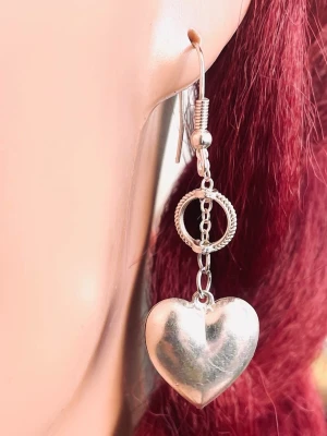 By prisförslag - 1 st Silvrigt örhängen med hjärthänge - Ett silvrigt örhänge med ett stort hjärthänge och en dekorativ ring ovanför. Örhänget har en blank finish och är tillverkade i metall. Perfekta för dig som gillar statement-smycken och vill ha något unikt.