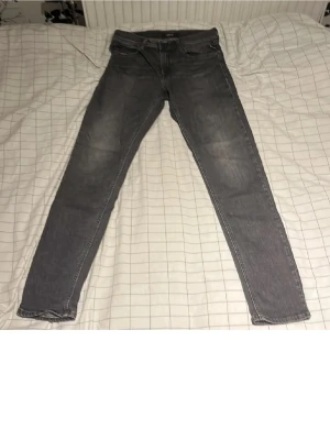 Grå slim fit jeans - Snygga grå slim fit jeans med klassisk femficksdesign och diskreta slitningar på låren. Jeansen har raka ben och normal midja, perfekta till en avslappnad stil. Tillverkade i mjukt denimtyg för skön känsla.