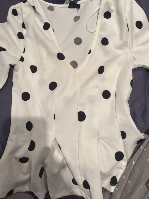 Vit blus med svarta prickar och v-ringning - Har sminkfläckar som jag inte testat att ta bort, de va så när jag köpte den. Kunde ej lämna tbx den pga det. Aldrig använt