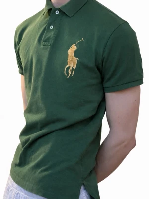 Ralph Lauren Pikè - Ralph Lauren Grön Pikétröja  En djupgrön Polo Ralph Lauren-piké med formad silhuett och finstrukturerat tyg, prydd med den ikoniska broderade ryttaren och en markant sifferpatch på ärmen.En mycket ovanlig modell som är svår att idag få tag på. Tyget faller naturligt och ger plagget en stillsam elegans. 