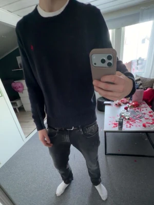 Mörkblå stickad tröja från Polo Ralph Lauren - Snygg mörkblå stickad tröja från Polo Ralph Lauren med klassisk röd logga broderad på bröstet. Tröjan har rund halsringning och ribbade muddar vid ärmslut och nederkant. Perfekt till jeans eller chinos för en clean look.