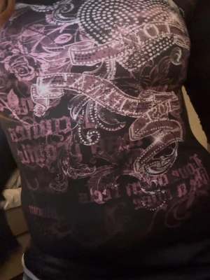 Svart långärmad topp med rosa tryck - Cool svart långärmad topp med rosa och vita grafiska tryck och mönster framtill. Slimmad passform och rund halsringning. Perfekt för dig som gillar edgy och detaljerade prints. Vit på insidan och sportigt material.