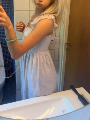 Ljuslila prickig klänning med volang - Hej!☀️Säljer denna söta ljuslila klänning med små vita prickar och volangdetaljer vid axelbanden. Klänningen har en lätt rynkad byst, smala axelband och faller i en mjuk, luftig form. Perfekt för sommarens varma dagar!💕Klänningen har några små tecken på användning på ett parti på ryggen (syns på bilden) men är inget som man tänker på! 