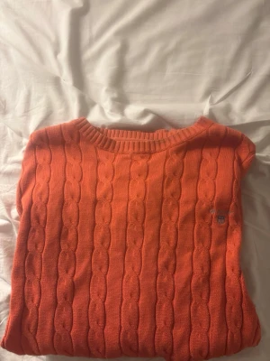 Orange kabelstickad tröja från Gant - Säljer en orange kabelstickad tröja från Gant i premium bomull. Tröjan har rund halsringning, ribbade muddar och Gant-logga broderad på bröstet. Perfekt för dig som gillar klassisk och stilren design med en färgklick.
