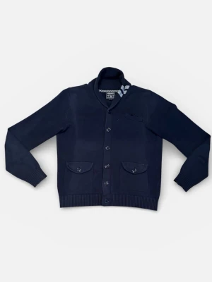 Cardigan från Woolrich - Mörkblå kofta från Scotch & Soda med knäppning framtill, två fickor med lock och knapp samt ribbade muddar vid ärmslut och nederkant. Snygg sjalkrage och diskret bröstficka för extra stilpoäng.