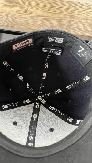 Svart New Era Yankees 59FIFTY keps - Säljer en svart New Era 59FIFTY keps med klassiskt New York Yankees-broderi framtill i vitt. Kepsen har broderad New Era-logga på sidan. Tillverkad i ett slitstarkt tyg som ger en clean och sportig look.  Storleken är 7 1/8 (56,8 cm)