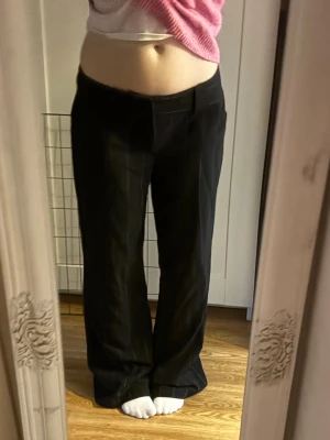 Svarta kostymbyxor med diskreta ränder - Säljer ett par svarta kostymbyxor med diskreta vertikala ränder. Byxorna har raka ben, låg midja och bälteshällor. Klassisk och stilren modell som passar perfekt till en trendig look. Materialet ser ut att vara en blandning av polyester och viskos.