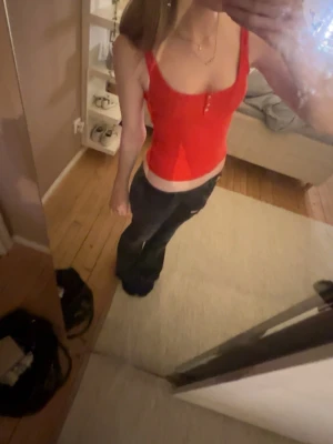 Röd ribbad linnetopp med knappar - Trendig röd linnetopp med smala axelband och knappdetaljer framtill. Toppen är ribbad och har en tight passform som framhäver figuren. Perfekt att styla med jeans eller kjol för en cool look.